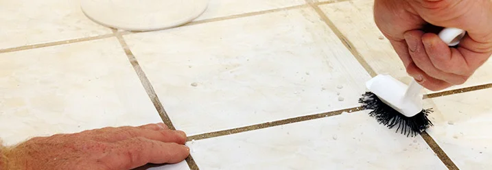 Hand reinigt Fliesenfugen mit Bürste